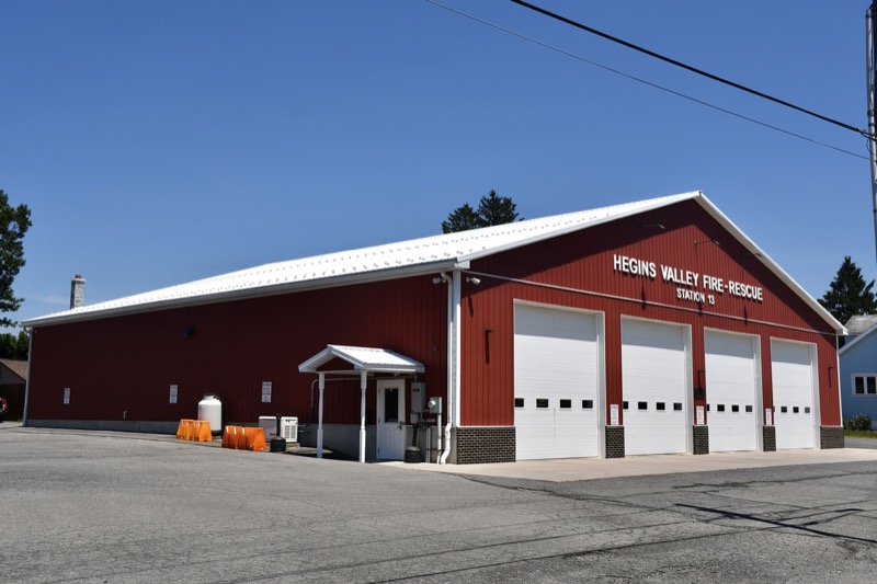Station 13 on a clear day: a red steel building with a white roof, four white bay doors and HEGINS VALLEY FIRE-RESCUE STATION 13 lettered on the front.