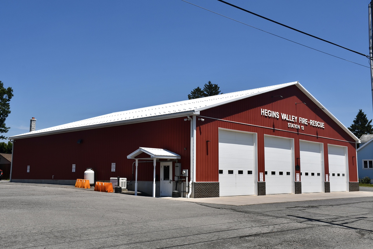Station 13 on a clear day: a red steel building with a white roof, four white bay doors and HEGINS VALLEY FIRE-RESCUE STATION 13 lettered on the front.
